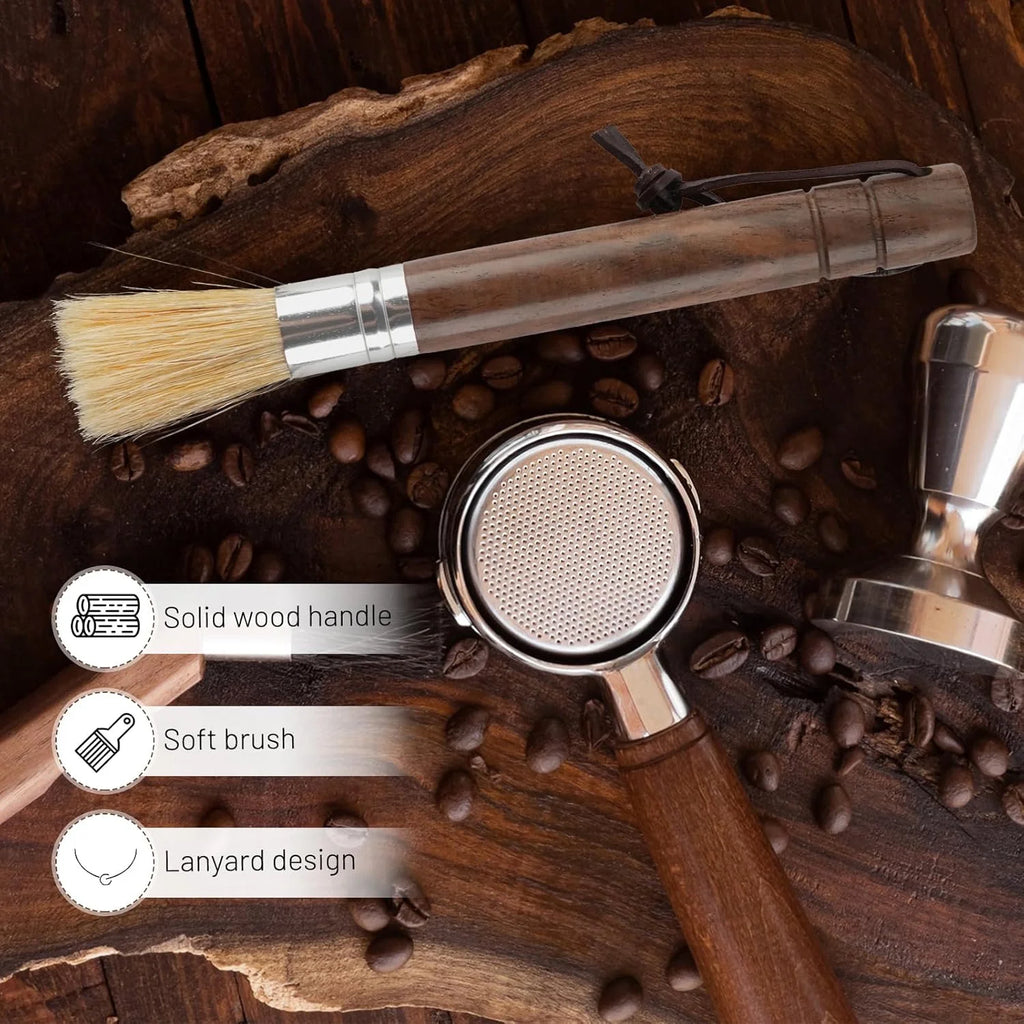 Solid wood handle espresso brush lying on dark wood next to coffee beans, tamper, and portafilter.