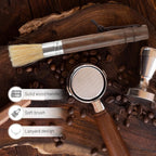 Solid wood handle espresso brush lying on dark wood next to coffee beans, tamper, and portafilter.