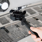 Barista using the counter-side group cleaner brush to scrub away stale coffee residues from the inner portafilter lock channel.