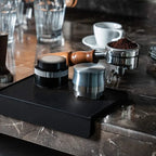 Heavy duty black silicone coffee tamper pad with 58mm portafilter, distributor and espresso accessories on marble countertop.