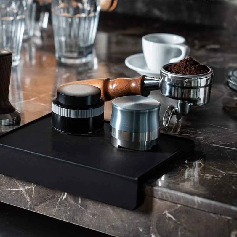 Heavy duty black silicone coffee tamper pad with 58mm portafilter, distributor and espresso accessories on marble countertop.