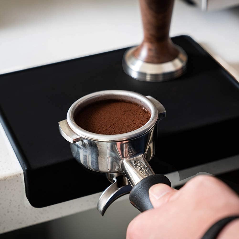 Perfectly leveled espresso coffee puck in stainless steel portafilter over black food-grade silicone mat.