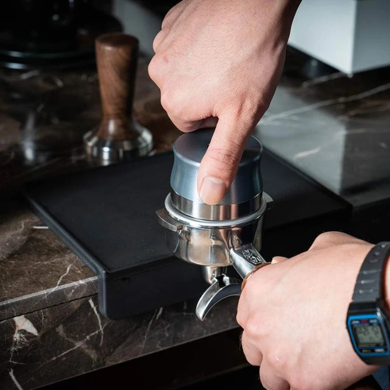 Barista pressing coffee grounds into portafilter on non-slip thick silicone edge mat protector.